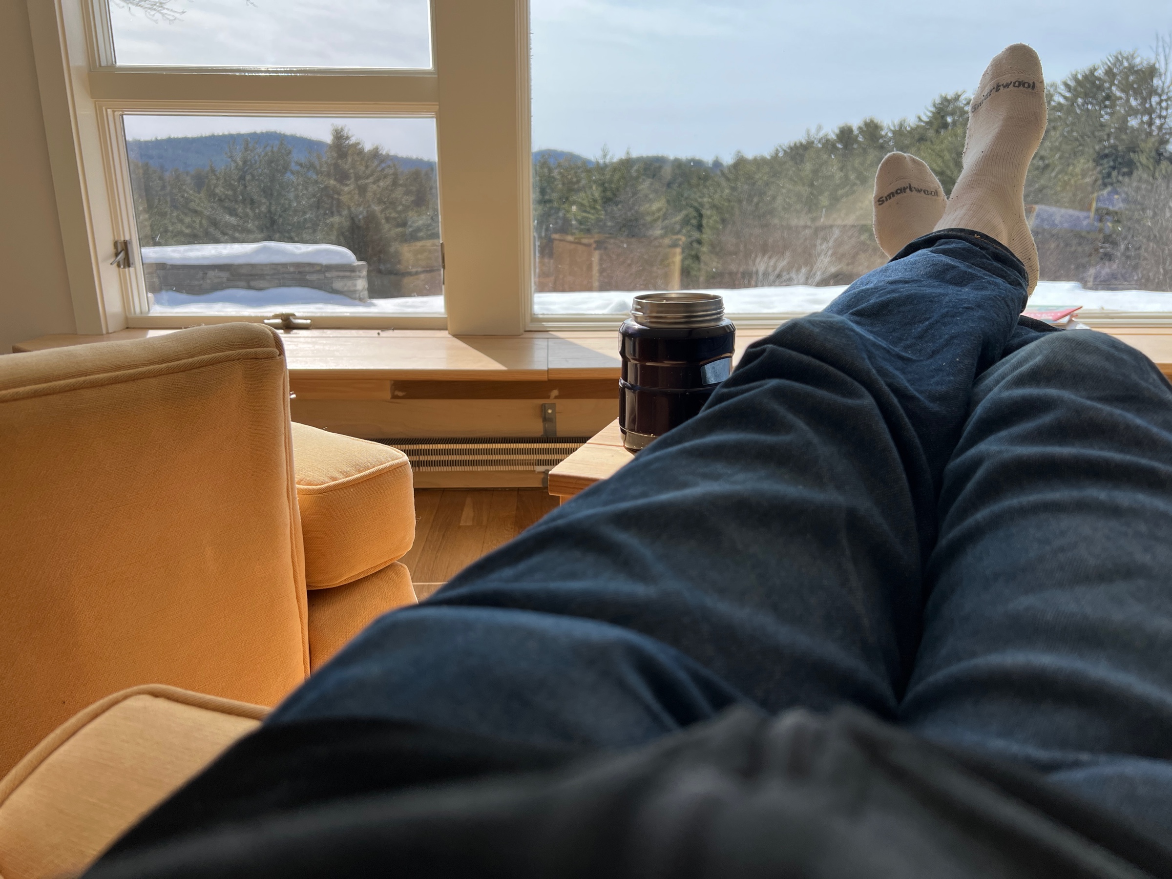 my feet up on an ottoman next to a cup of coffee with a view of a snowy patio and forest in the background