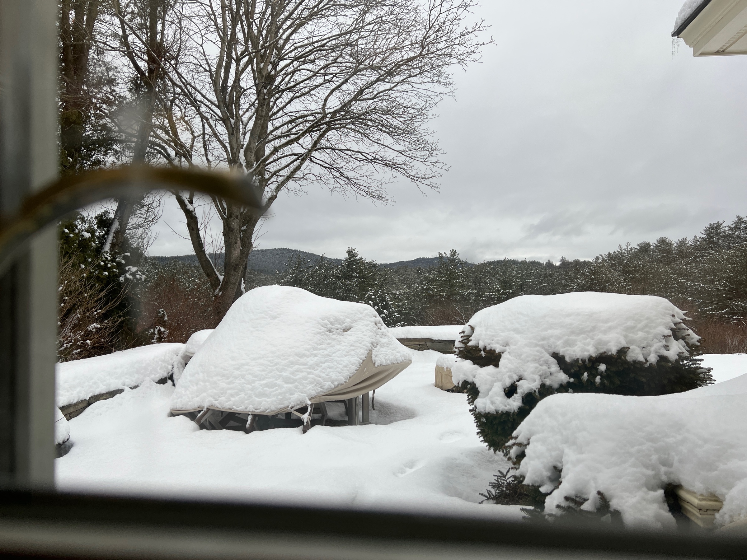 snow-covered patio furniture seen through a window pane with blurry door handle at left