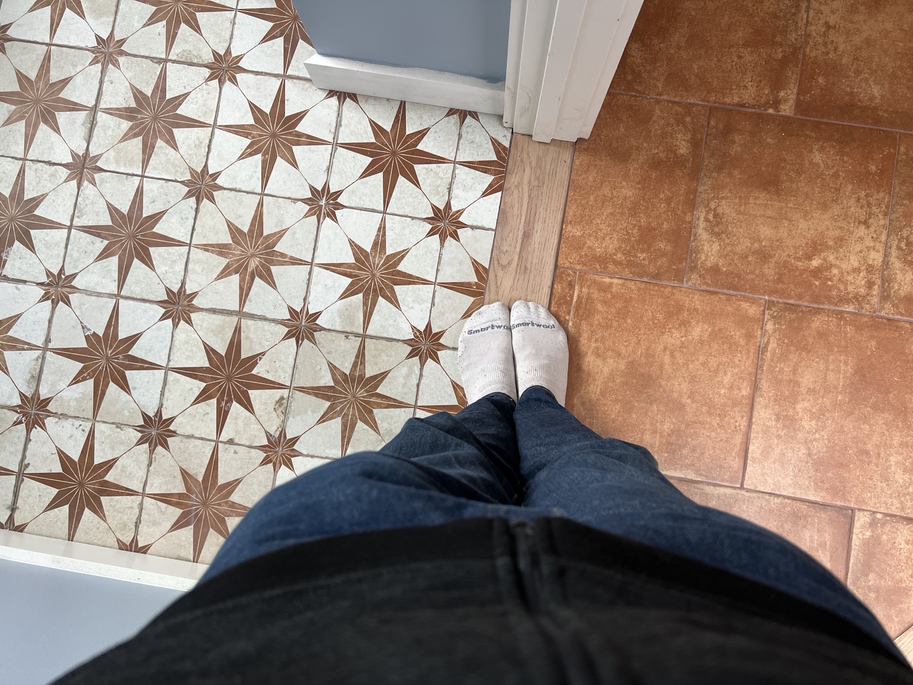 camera pointing at photographer's feet standing between two rooms with tiled floors